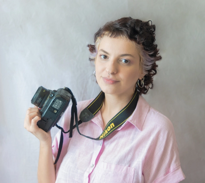 Foto da fotógrafa e proprietária da Casulo Fotografias, Eulália Lins, sorrindo e segurando sua câmera.