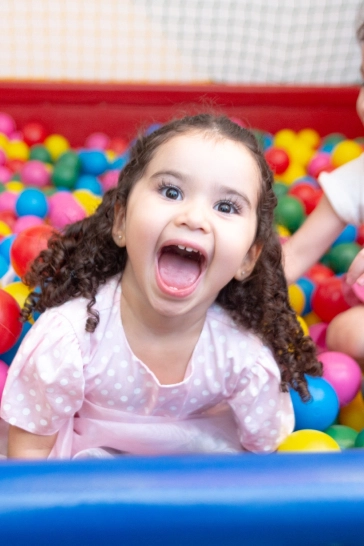 Garotinha extremamente feliz numa piscina de bolinhas em sua festa de aniversário.