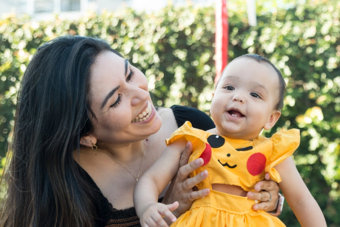 Mãe segurando e admirando a filha bebê, ambas sorrindo.