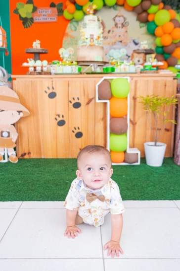 Guilherme engantinhando de frente a mesa do bolo do seu aniversário, em direção a fotógrafa.