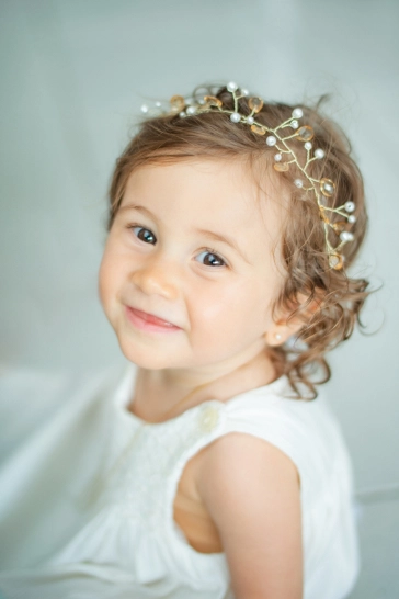 Clara, sentada no chão e com uma linda tiara, olha para cima em direção a câmera e mostra seu sorriso.