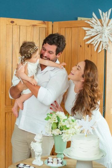 Clara e seus pais se divertindo junto à mesa do bolo da festa de batizado.